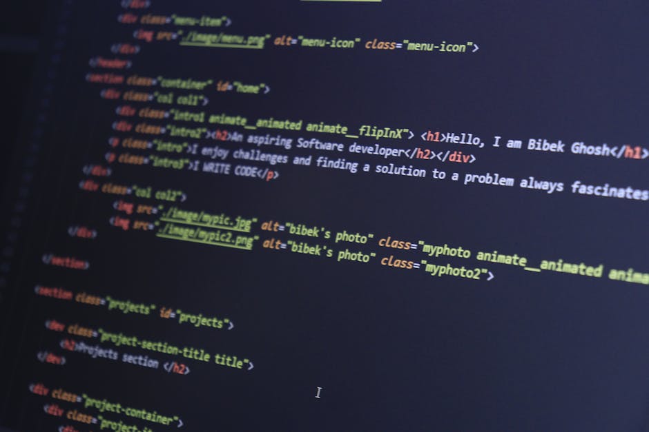 A person working on a laptop computer displaying a dark-themed code editor with syntax-highlighted lines, situated on a table in an indoor environment. The individual's hands are active, with one hand